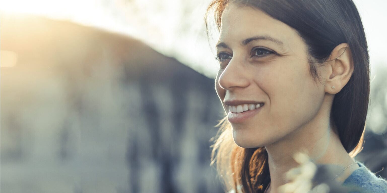 Closeup of a smiling young woman looking into the distance at sunset. Wide photo with copy space.
